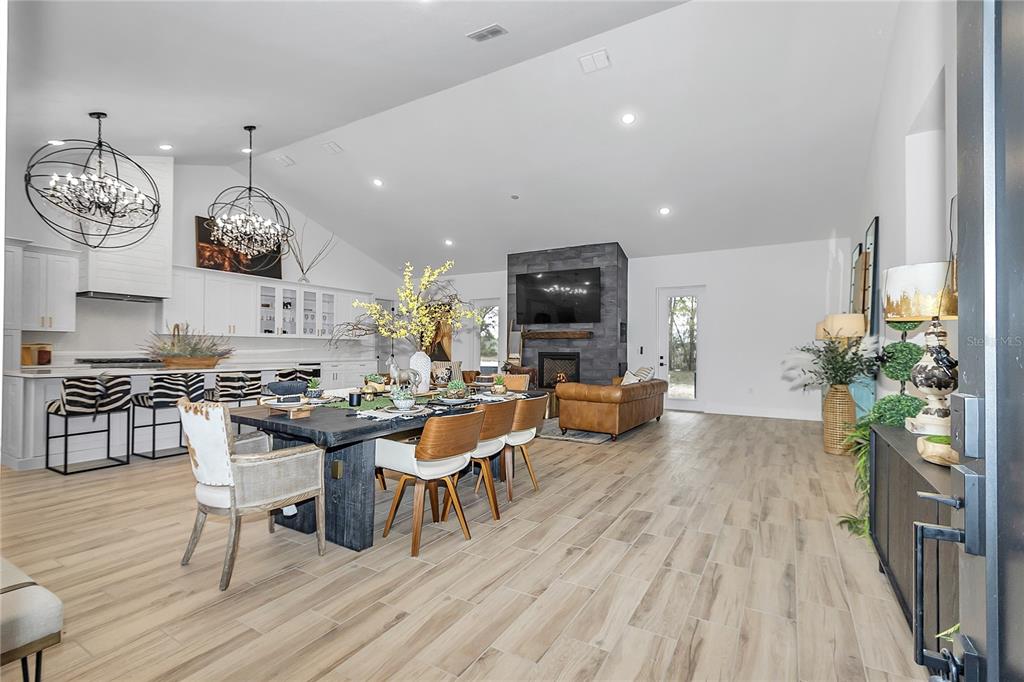 An open-concept living and dining area features a stone fireplace, wood-look tile flooring, and chandeliers — 3750 SE 139TH TERRACE, MORRISTON, FL