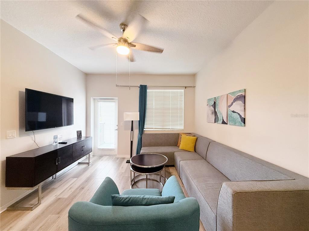 A living room features a grey sectional sofa, a teal armchair, and a dark media console — 4013 BREAKVIEW DRIVE UNIT A308, ORLANDO, FL