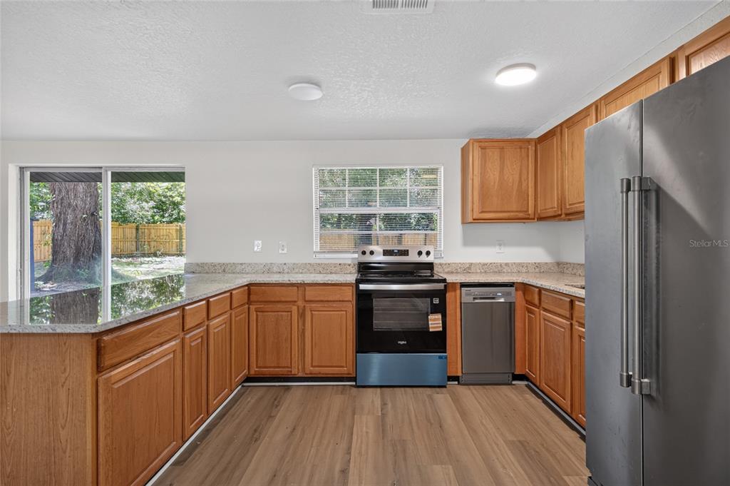 An empty room with light wood-look flooring, a ceiling fan, a window, and a closed door — 26356 ROLLING ACRES DRIVE, BROOKSVILLE, FL