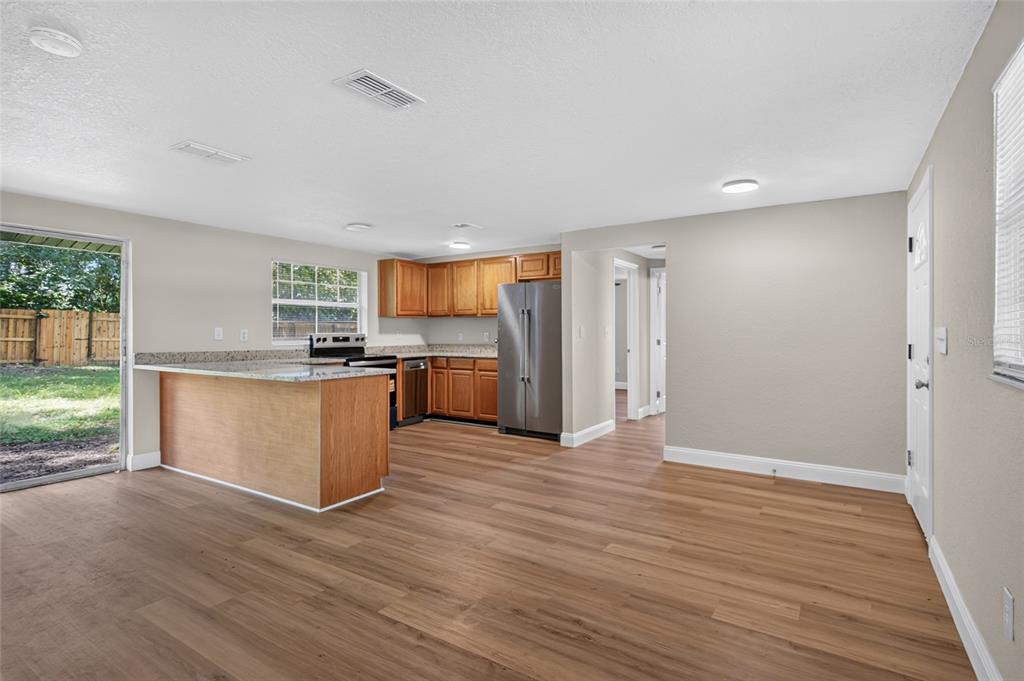 A kitchen features wood cabinets, granite countertops, stainless steel appliances, and light wood-look flooring — 26356 ROLLING ACRES DRIVE, BROOKSVILLE, FL