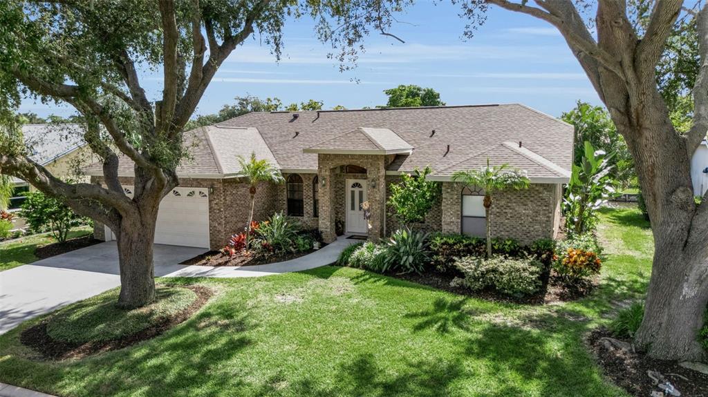 A single-story brick house with a two-car garage, arched entryway, and mature trees in front — 4739 SPRING MEADOW LANE, SARASOTA, FL