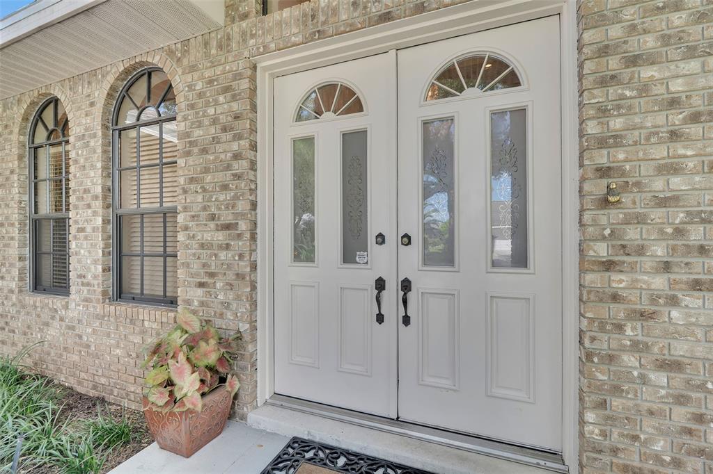 A light-colored double front door with glass inserts sits in a tan brick exterior wall — 4739 SPRING MEADOW LANE, SARASOTA, FL