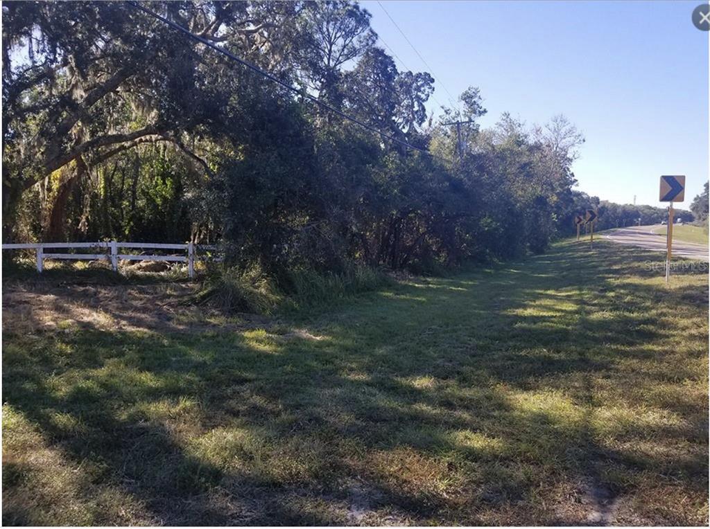 A grassy roadside area features a white fence, dense trees, and yellow road signs — 2819 SAFFOLD ROAD, WIMAUMA, FL