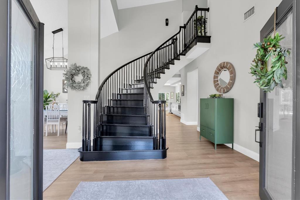A foyer features a curved black staircase, light wood flooring, and a green storage cabinet — 1625 PERCHERON DRIVE, TRINITY, FL
