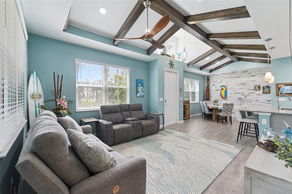 A living room with vaulted ceilings, exposed wood beams, and blue walls features gray furniture — 384 GYPSY PALACE LANE, DAYTONA BEACH, FL