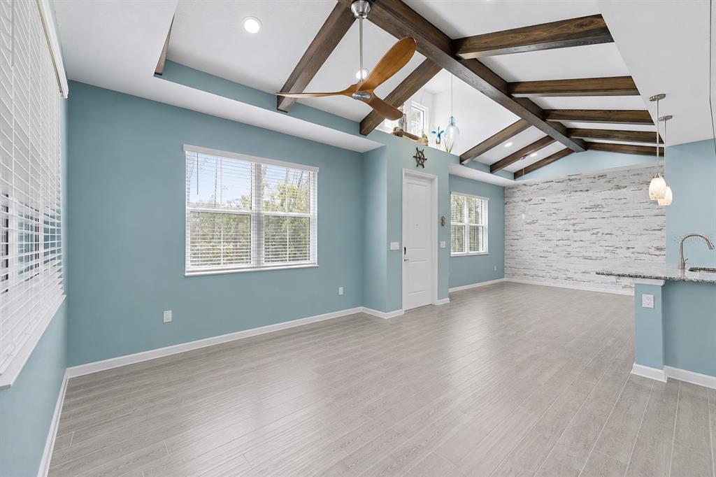 A living room with light blue walls, wood ceiling beams, and a white brick accent wall — 384 GYPSY PALACE LANE, DAYTONA BEACH, FL