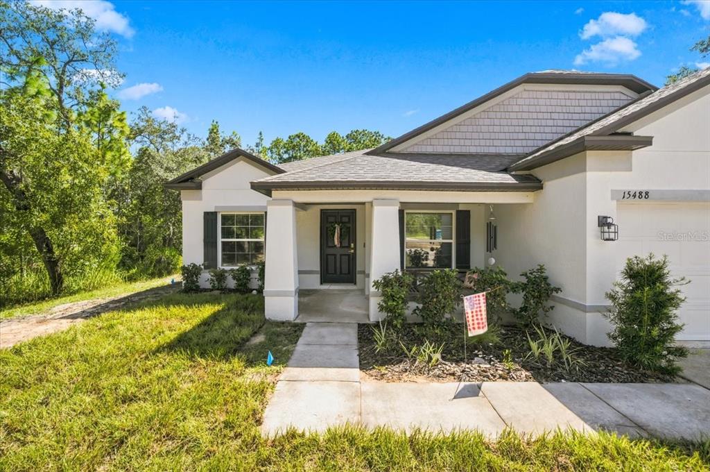 A single-story house with a white stucco exterior, a covered entryway, and a front lawn — 15488 SCOLDER LOOP, WEEKI WACHEE, FL