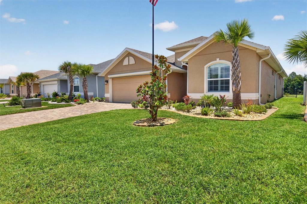 A tan house with a two-car garage, a paved driveway, and a palm tree out front — 37 LAGOON WAY, PALM COAST, FL
