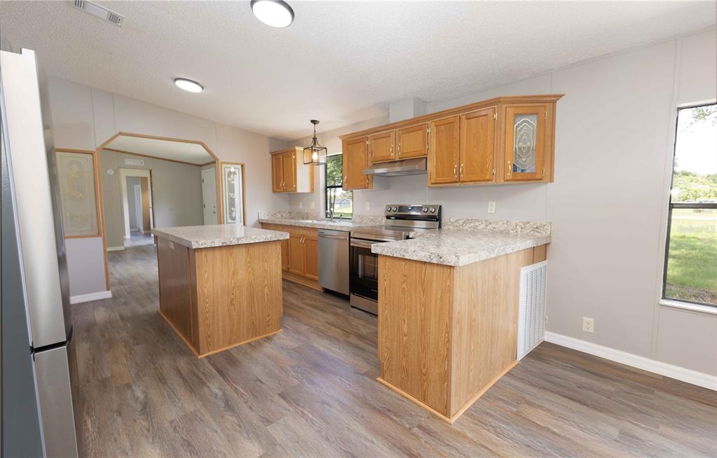 An empty living room features light-colored walls, wood-look flooring, a ceiling fan, and two windows — 968 CR222 ROAD, OXFORD, FL