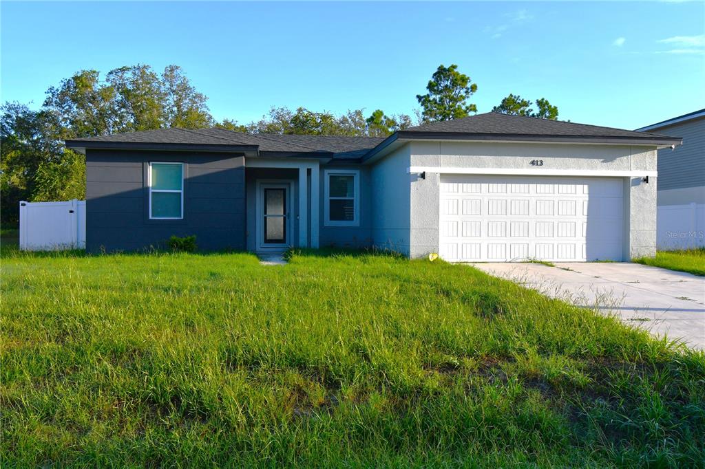 A single-story house with a two-car garage and a front yard with tall grass — 413 ST JOHNS LANE, POINCIANA, FL