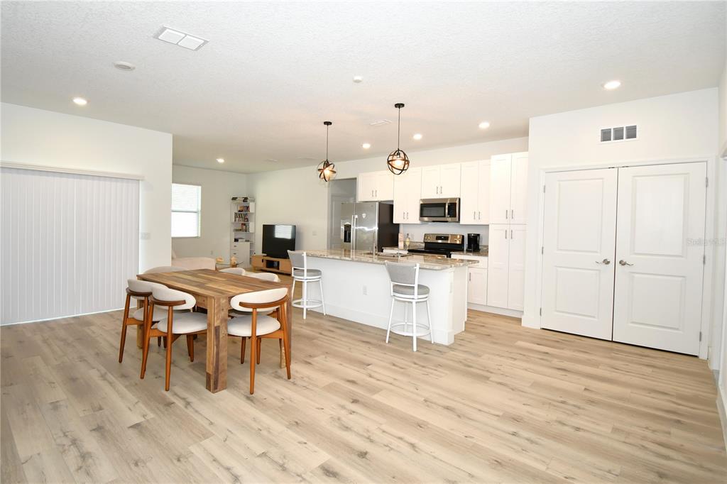 An open-concept kitchen and dining area with white cabinetry, wood-look flooring, and a center island — 413 ST JOHNS LANE, POINCIANA, FL