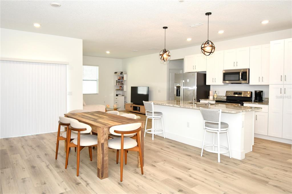 An open-concept kitchen and dining area featuring white cabinets, a granite island, and wood flooring — 413 ST JOHNS LANE, POINCIANA, FL