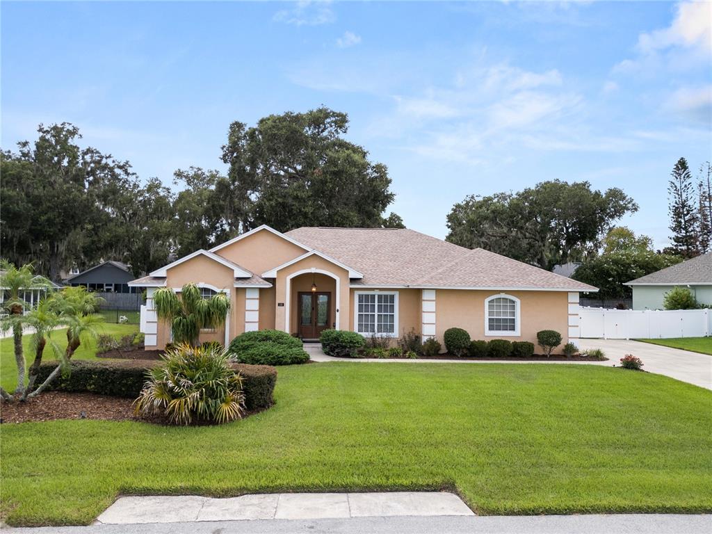 A single-story tan house with a shingled roof and a manicured front lawn — 318 HAMILTON SHORES DRIVE NE, WINTER HAVEN, FL