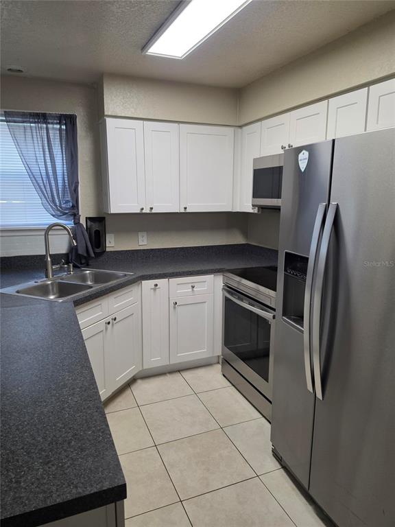 A kitchen features white cabinets, dark countertops, stainless steel appliances, and light-colored floor tiles — 3019 ANTIQUE OAKS CIRCLE UNIT 127, WINTER PARK, FL