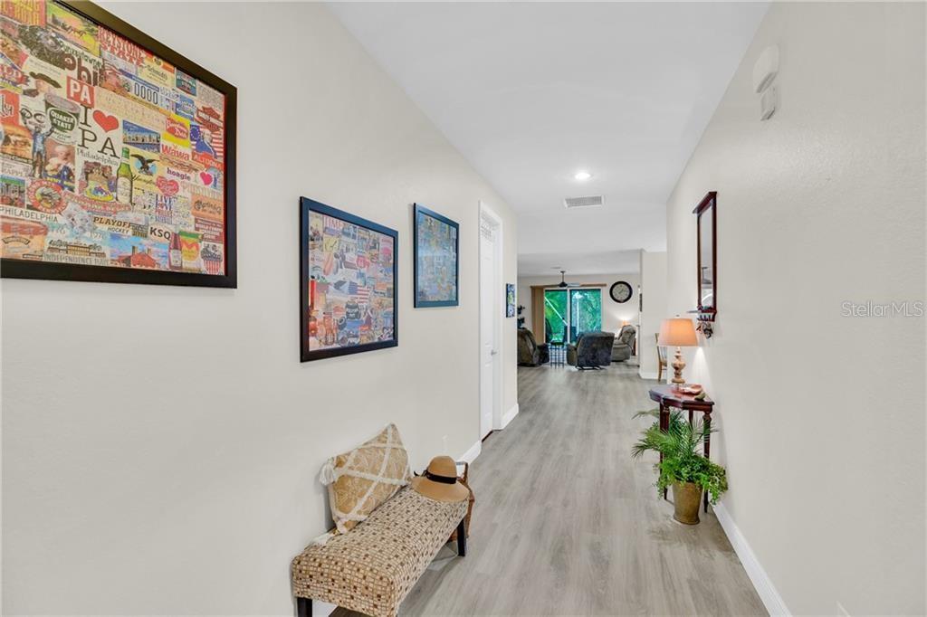 A hallway with light wood-look flooring leads to an open living area with sliding glass doors — 3189 ASTOR AVENUE, VERO BEACH, FL