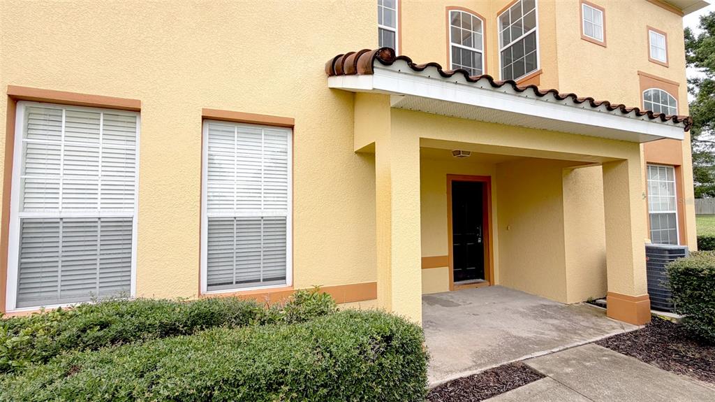 The exterior of a yellow two-story building features a covered entryway and white-framed windows — 203 MADISON CIRCLE, DAVENPORT, FL