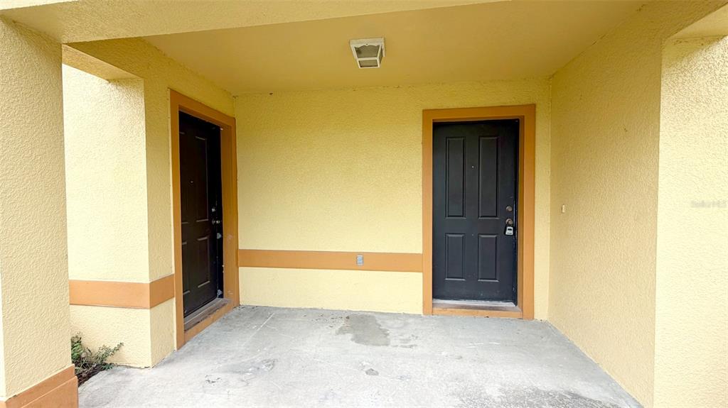 A covered concrete entryway features two dark doors set into yellow stucco walls — 203 MADISON CIRCLE, DAVENPORT, FL