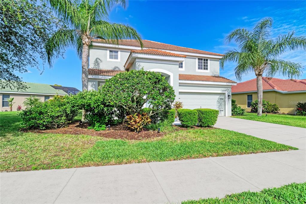 A two-story suburban house with a light-colored stucco exterior, a tile roof, and palm trees — 9035 WILLOWBROOK CIRCLE, BRADENTON, FL