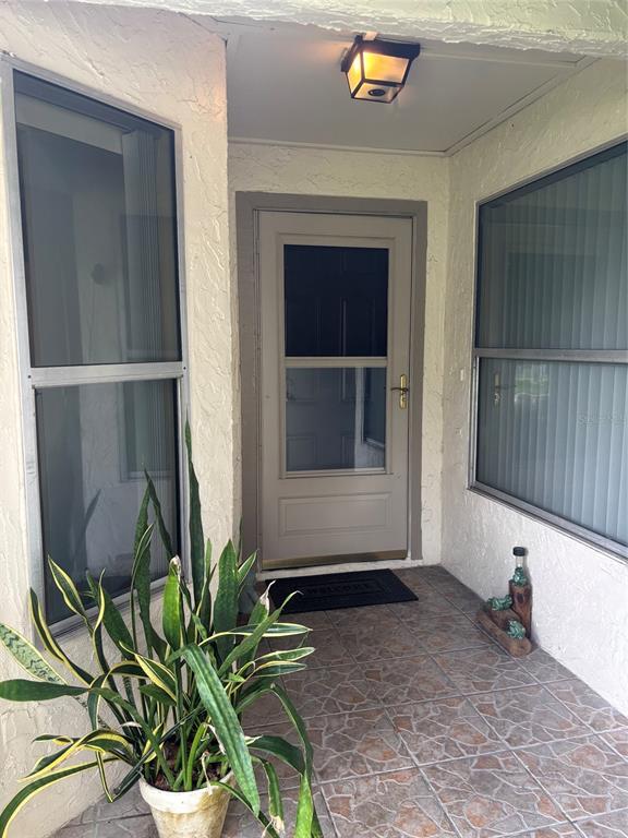 A covered entryway features a light-colored front door, tiled flooring, and a potted snake plant — 283 HILL STREET UNIT 283, CASSELBERRY, FL