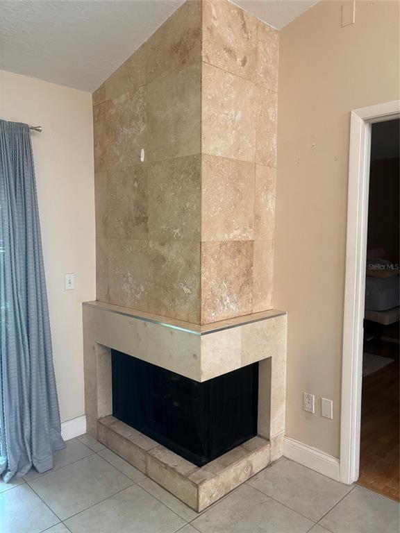 A corner fireplace features tan travertine tile surround and a raised hearth in a room — 283 HILL STREET UNIT 283, CASSELBERRY, FL