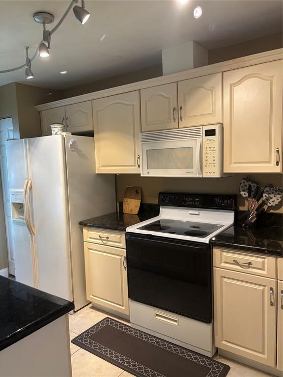 A kitchen features cream-colored cabinets, black countertops, a white refrigerator, and a black electric stove — 283 HILL STREET UNIT 283, CASSELBERRY, FL