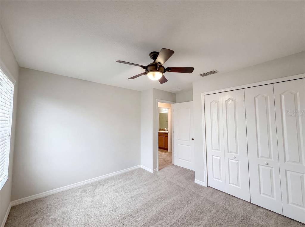 A bedroom with light gray walls, beige carpet, a ceiling fan, and white closet doors — 1308 SEBURN ROAD, APOPKA, FL