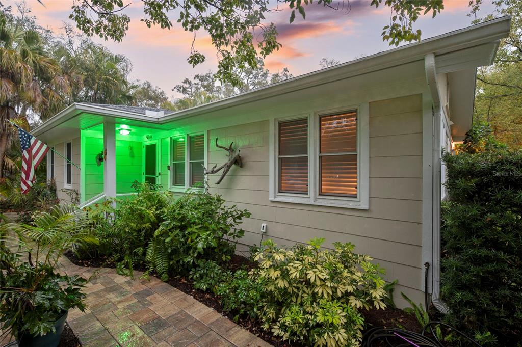 A single-story house exterior with light siding, a stone walkway, and green porch lighting — 501 BROADWAY, DUNEDIN, FL