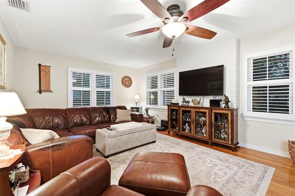 A living room features a leather sectional, a brick fireplace with a television, and shutters — 501 BROADWAY, DUNEDIN, FL