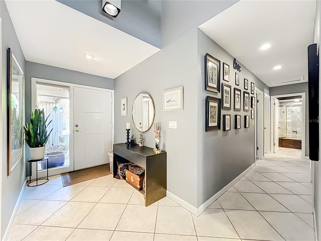 A bright entryway features light gray walls, tiled floors, a console table, and a gallery wall — 104 JUNIPER LANE, LONGWOOD, FL