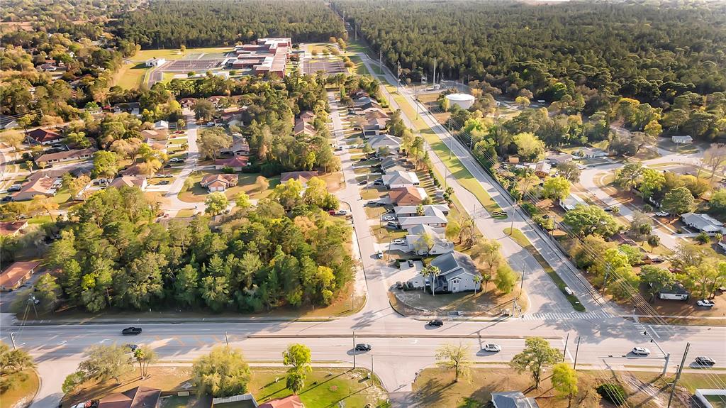 An aerial view shows a suburban neighborhood with houses, streets, and a large wooded area — 4380 AZORA ROAD, SPRING HILL, FL