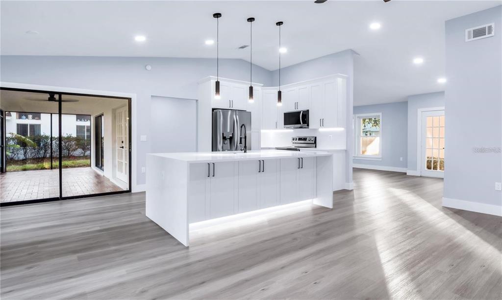 A modern kitchen features white cabinetry, a large island with under-cabinet lighting, and wood-look flooring — 1007 NW 82ND STREET, BRADENTON, FL