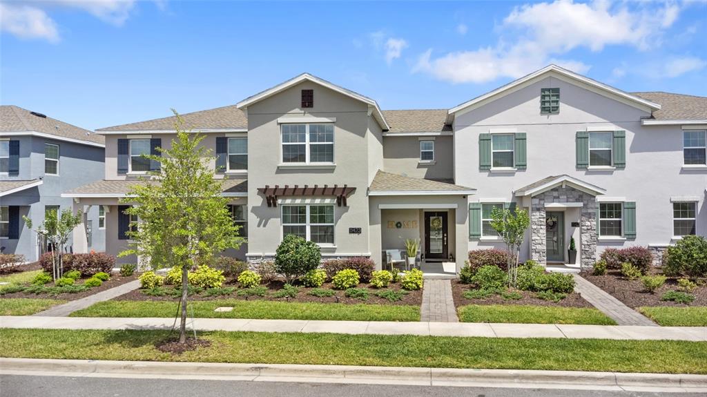 A two-story townhouse exterior features light-colored stucco, stone accents, and a covered front entryway — 11473 LISTENING DRIVE, ORLANDO, FL