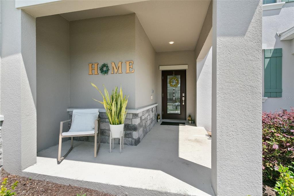 A covered front porch features a rocking chair, a potted plant, and a front door — 11473 LISTENING DRIVE, ORLANDO, FL