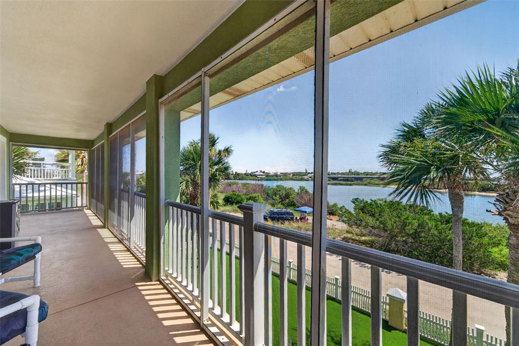 A screened-in balcony overlooks a body of water, palm trees, and a distant bridge — 9138 JUNE LANE, ST AUGUSTINE, FL