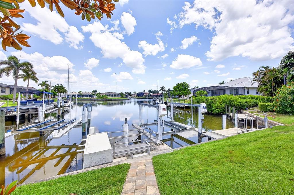 A canal-side backyard features a boat dock with a lift, a stone walkway, and palm trees — 3866 TURTLE DOVE BOULEVARD, PUNTA GORDA, FL