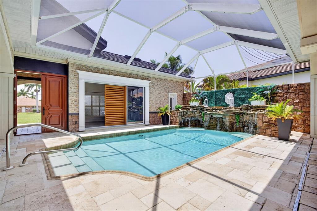 A screened-in swimming pool area features a stone waterfall, travertine decking, and a sliding door — 3866 TURTLE DOVE BOULEVARD, PUNTA GORDA, FL