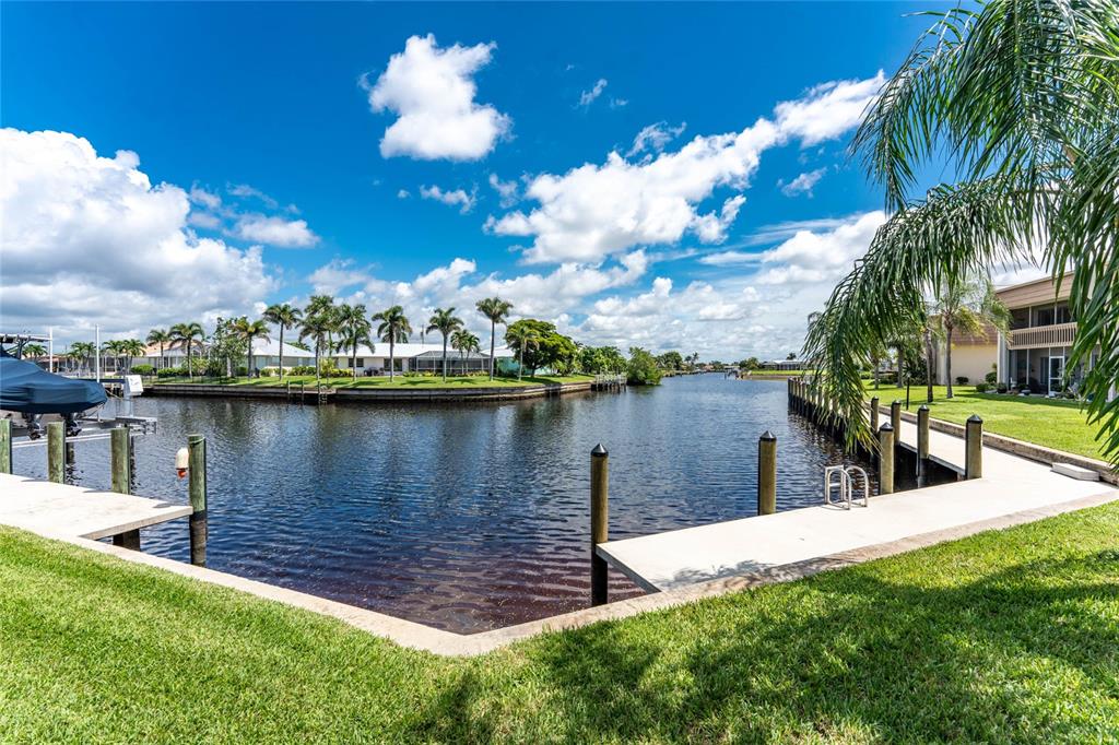 A canal view from a grassy backyard featuring a concrete dock and palm trees — 1080 BAL HARBOR BOULEVARD UNIT 7C, PUNTA GORDA, FL