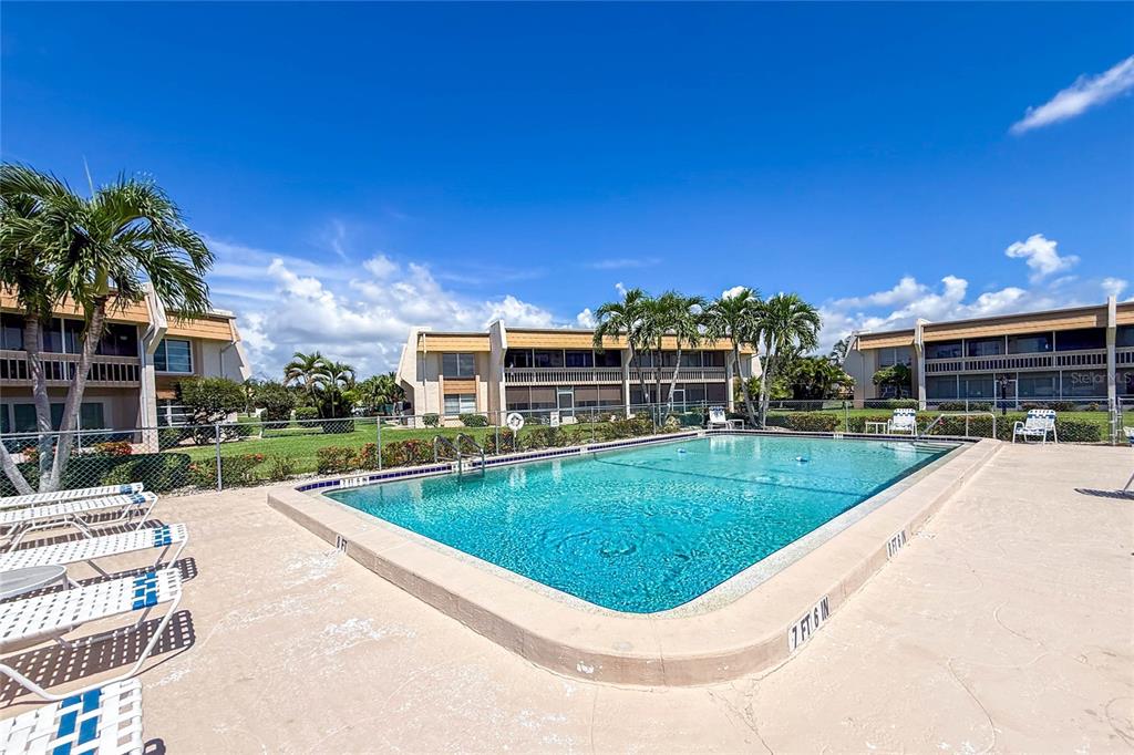An outdoor swimming pool is surrounded by a concrete deck and multi-story apartment buildings — 1080 BAL HARBOR BOULEVARD UNIT 7C, PUNTA GORDA, FL