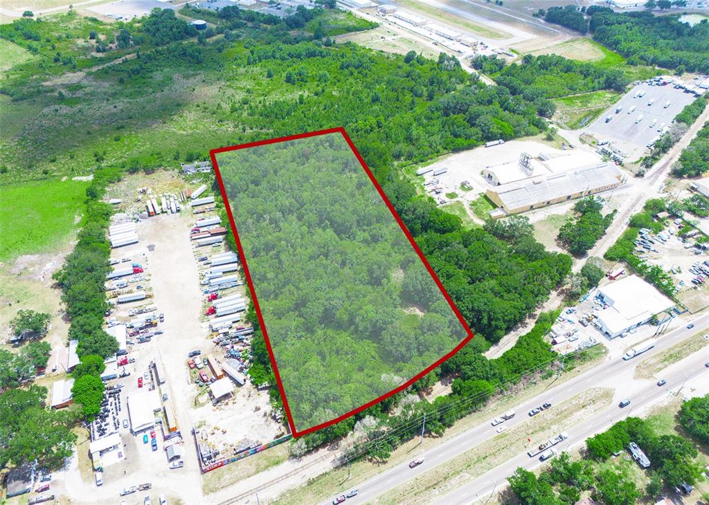 An aerial view shows a rectangular, tree-covered lot outlined in red next to industrial properties — SR-60, LAKE WALES, FL