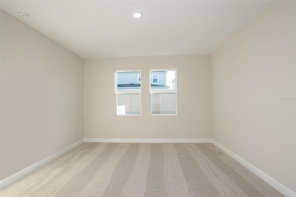 An empty bedroom features beige walls, light-colored carpet, and two windows — 33554 HAMMOCK BEACH WAY, DADE CITY, FL