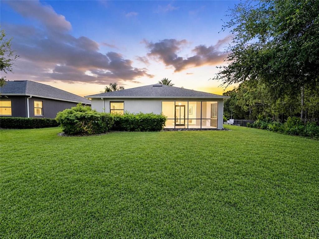 The back exterior of a single-story house features a screened-in lanai and a grassy yard — 2220 BARRINGTON LOOP, DAVENPORT, FL