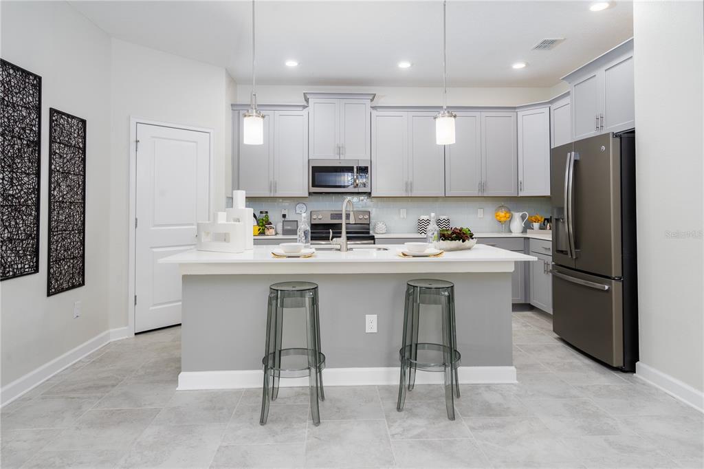 A modern kitchen features a central island with two stools, gray cabinetry, and stainless appliances — 2220 BARRINGTON LOOP, DAVENPORT, FL