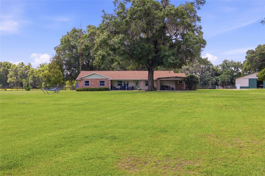 A single-story brick house with a large tree in the front yard and a carport — 13551 NE 14TH AVENUE, CITRA, FL
