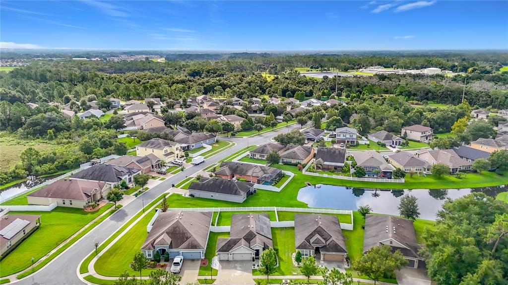 An aerial view shows a suburban neighborhood with houses, green lawns, and a small pond — 6328 SPARKLING WAY, WESLEY CHAPEL, FL