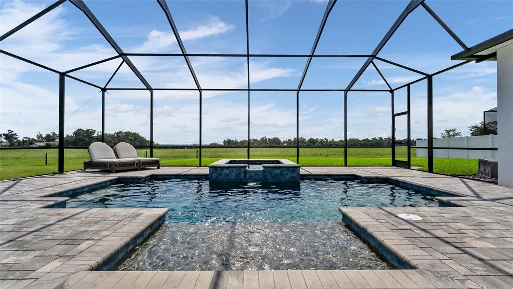 A screened-in patio features a swimming pool with a spillover spa and stone pavers — 7034 BENTRIDGE DRIVE, LAKELAND, FL