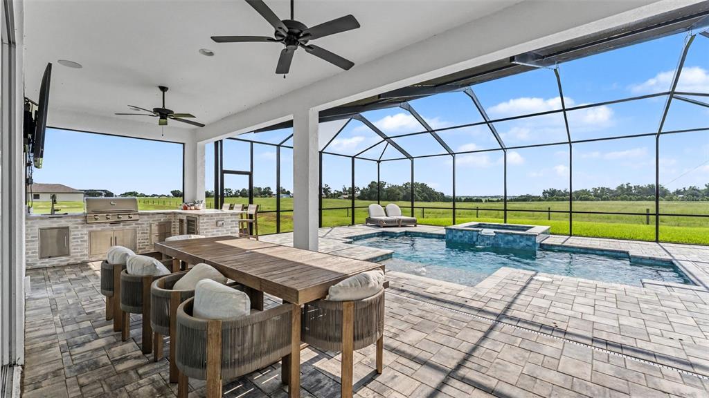 A covered patio features an outdoor kitchen, dining set, and a screened-in pool and spa — 7034 BENTRIDGE DRIVE, LAKELAND, FL