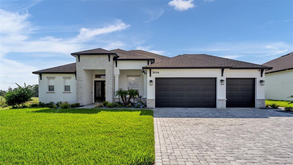 A modern single-story house with a white exterior, stone accents, and a paved driveway — 7034 BENTRIDGE DRIVE, LAKELAND, FL