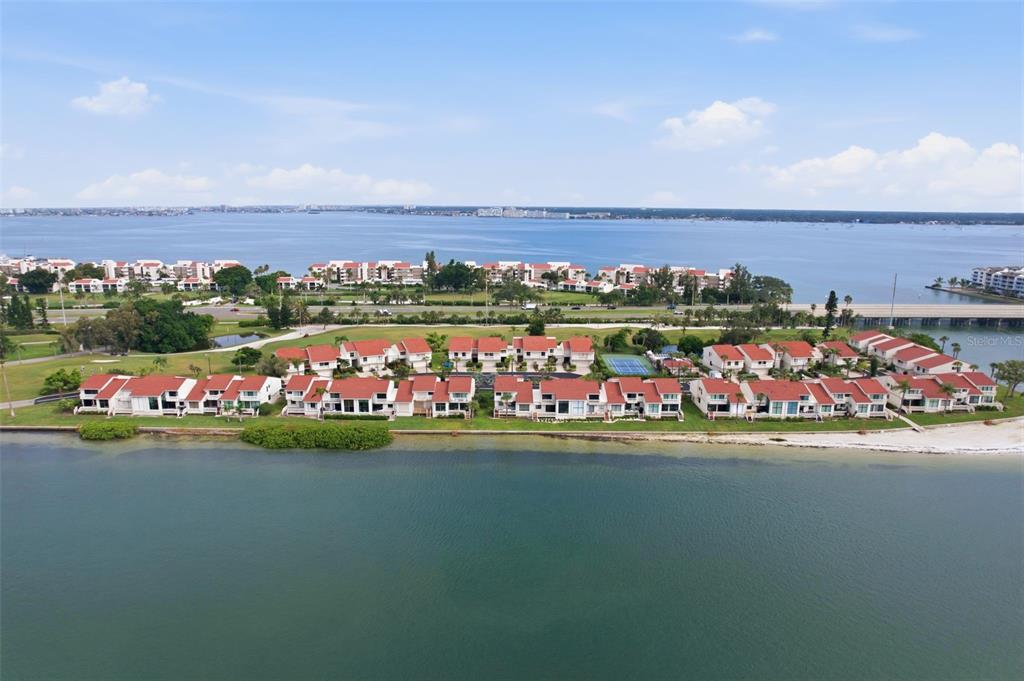An aerial view of a waterfront residential complex with red-roofed townhomes and a tennis court — 5619 ESCONDIDA BOULEVARD S, ST PETERSBURG, FL