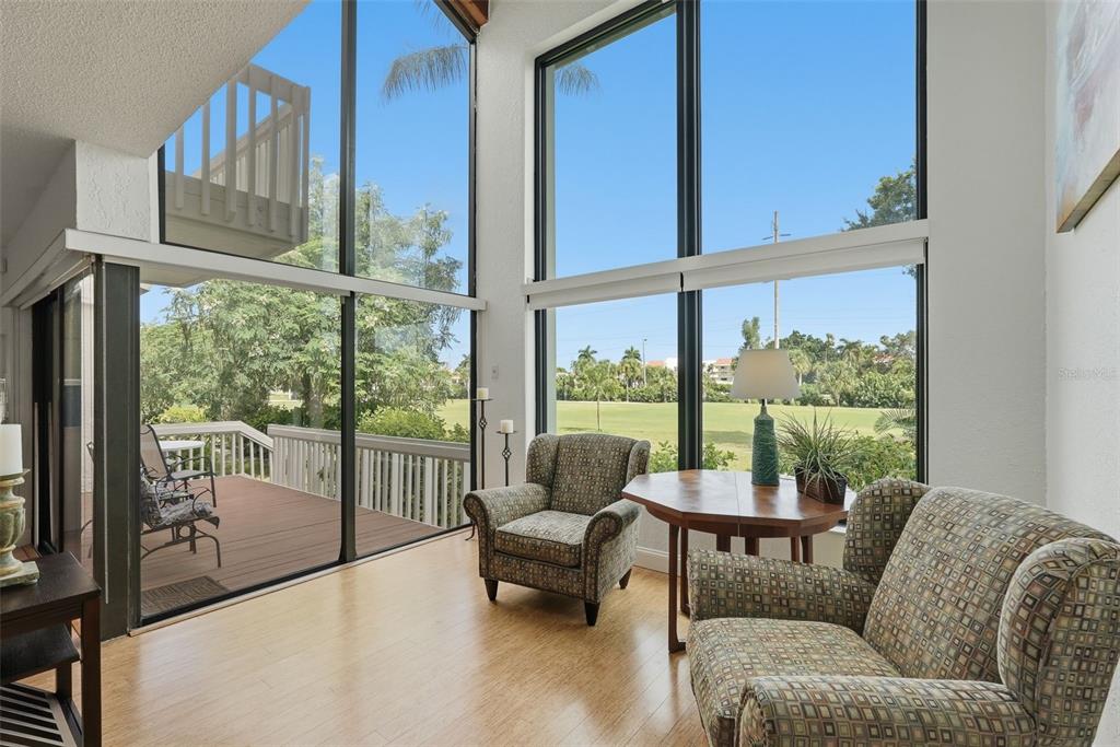 A living area features floor-to-ceiling windows, wood flooring, two patterned armchairs, and a deck view — 5619 ESCONDIDA BOULEVARD S, ST PETERSBURG, FL