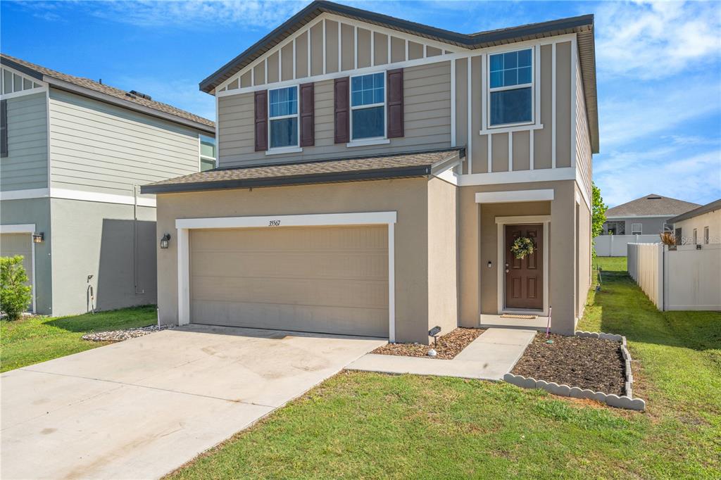 A two-story house with a beige stucco exterior, a two-car garage, and a brown door — 35567 BUTTONWEED, ZEPHYRHILLS, FL